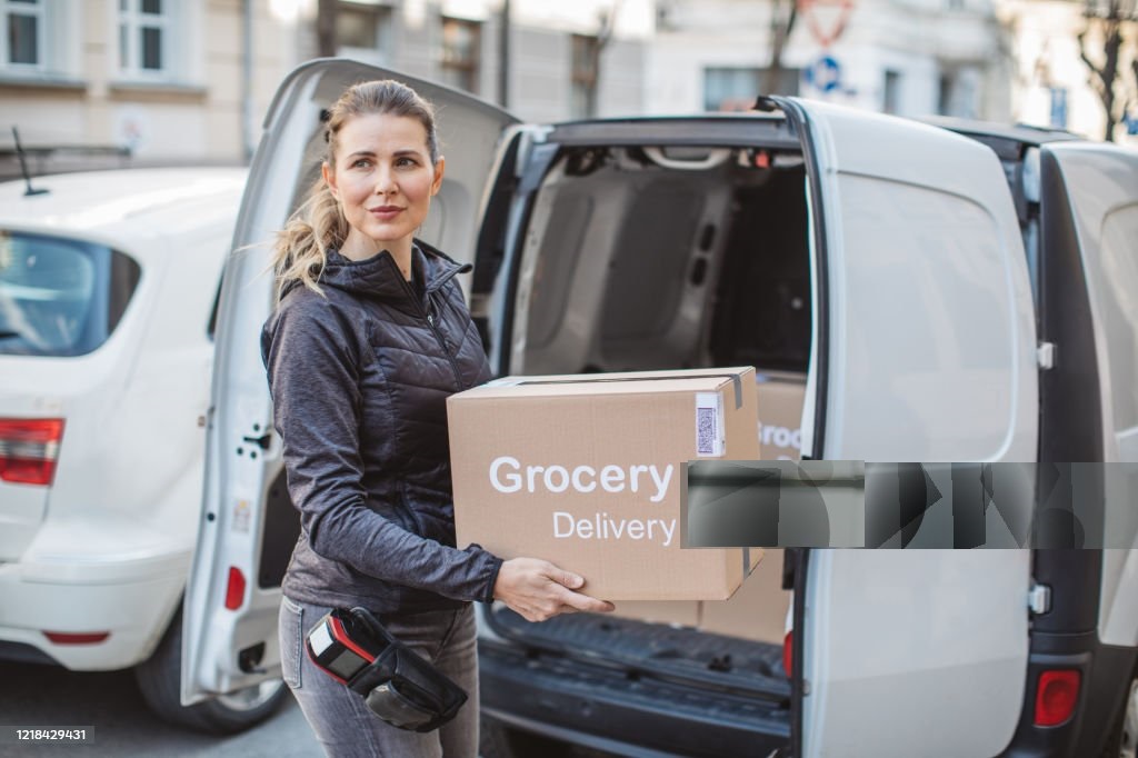 Delivering food ordered online while in home isolation during quarantine. Stay home we deliver sign on box. Unloading packages from car for customer