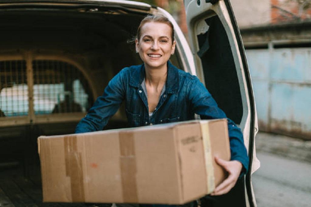 Young woman wearing a uniform delivering packages in a white van on a sunny day in the city street